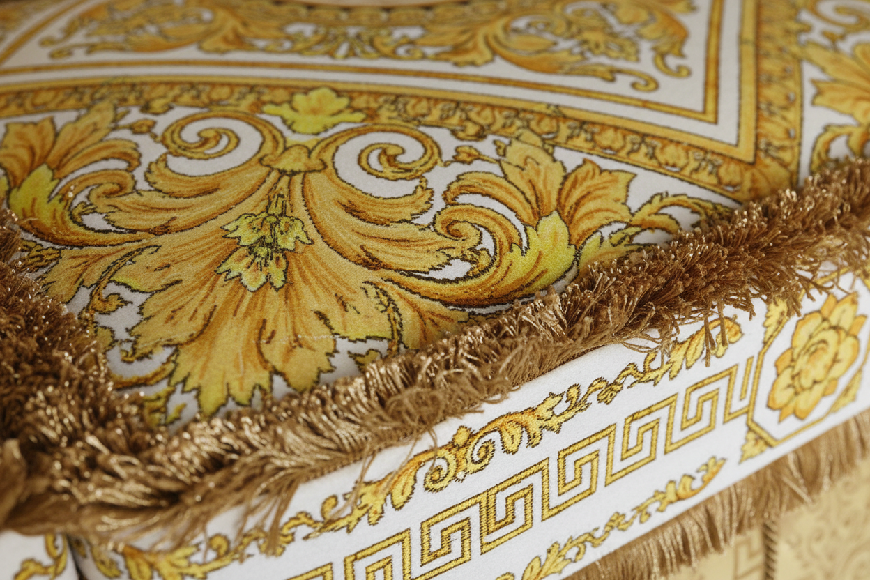 Macro detail of Versace Carre White Gold Z7010 velvet fabric with baroque floral and Medusa Greca pattern in gold, white and champagne tones with gold fringe trim